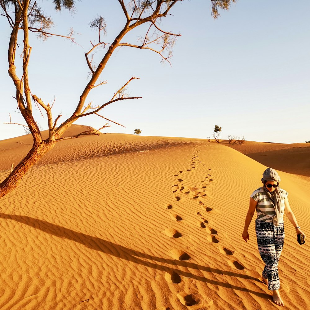 woman walking in brown sand dune leaving footprints in sand