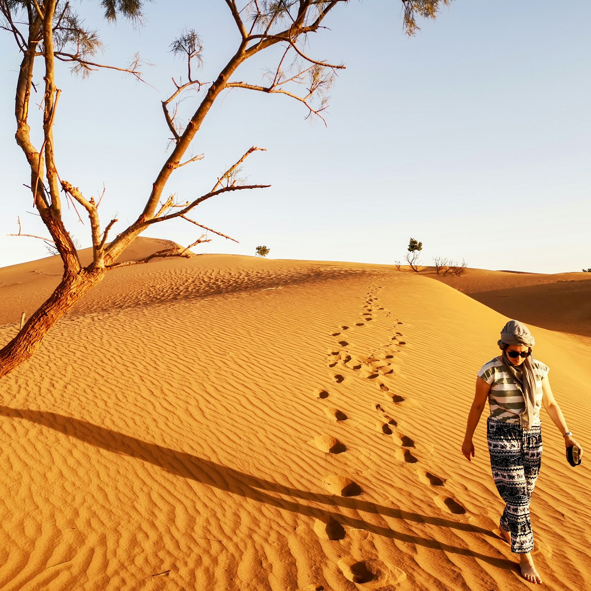 woman walking in brown sand dune leaving footprints in sand