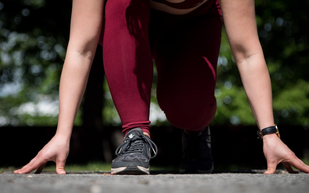 woman in maroon leggings and pair of black Nike sneakers squatting on starting line