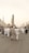 A large group of people dressed in white traditional garments walk towards an ornate architectural structure. The scene includes several tall minarets in the background under a clear, light-colored sky, suggesting a religious or cultural gathering.