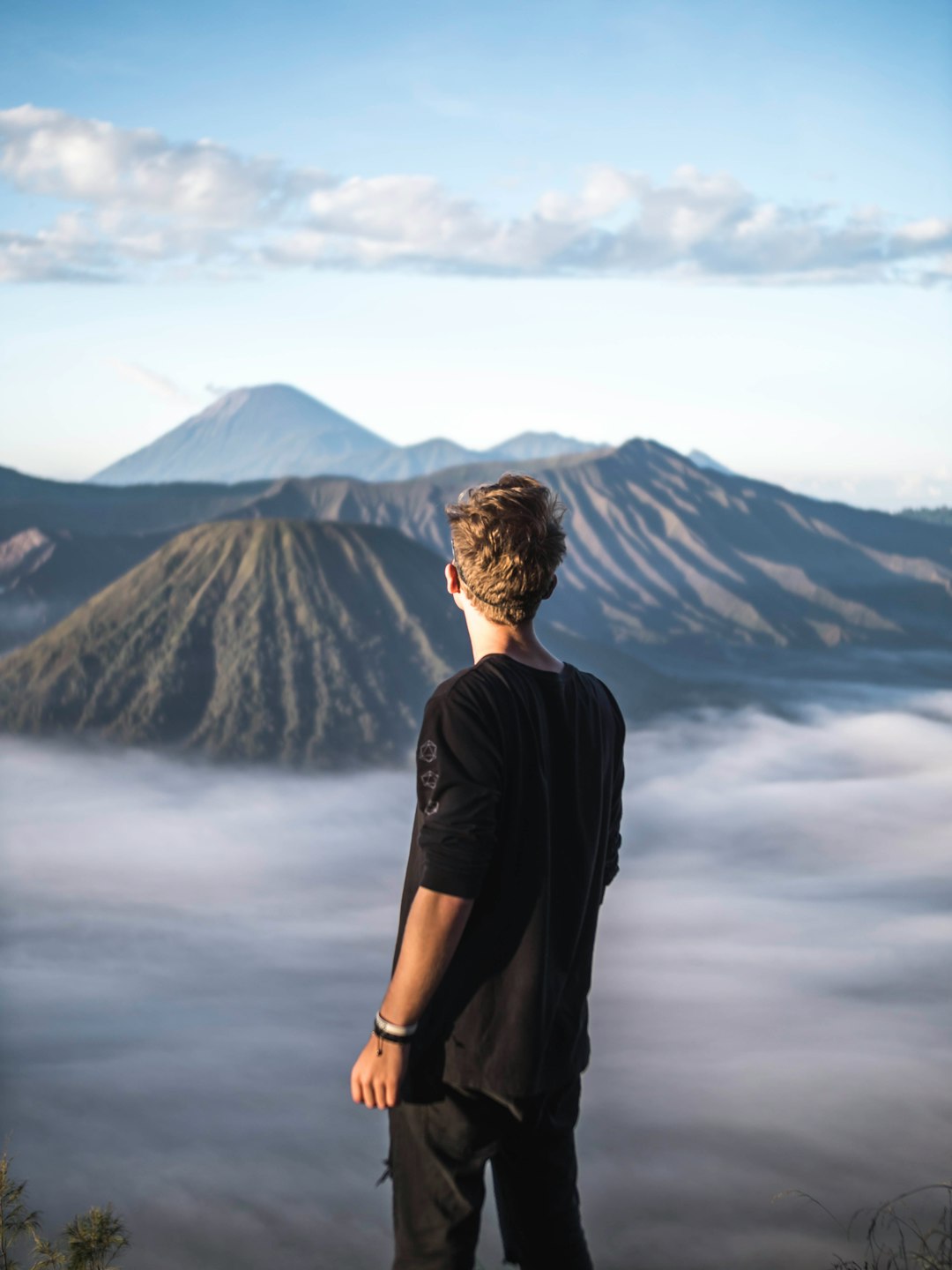 man standing and facing on mountain under blue and white skies