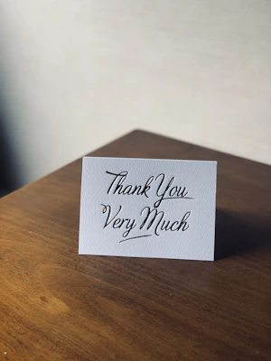 Glossy thank you card with minimalist black and gold design placed on a wooden table