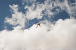 An airplane soaring above clouds with a subtle world map overlay in the background.