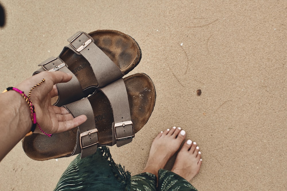 person holding pair of brown-and-black open toe sandals