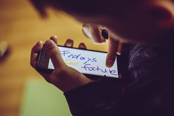 A person is holding a smartphone with a digital note that reads 'Fridays for Future' written in colorful handwriting. Fingers are interacting with the phone screen, which is brightly illuminated, contrasting with the darker surroundings.