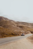 A scenic highway cutting through rolling hills with a Sandu Transport vehicle driving along.
