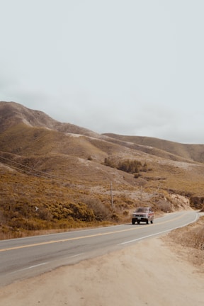 A scenic highway cutting through rolling hills with a Sandu Transport vehicle driving along.