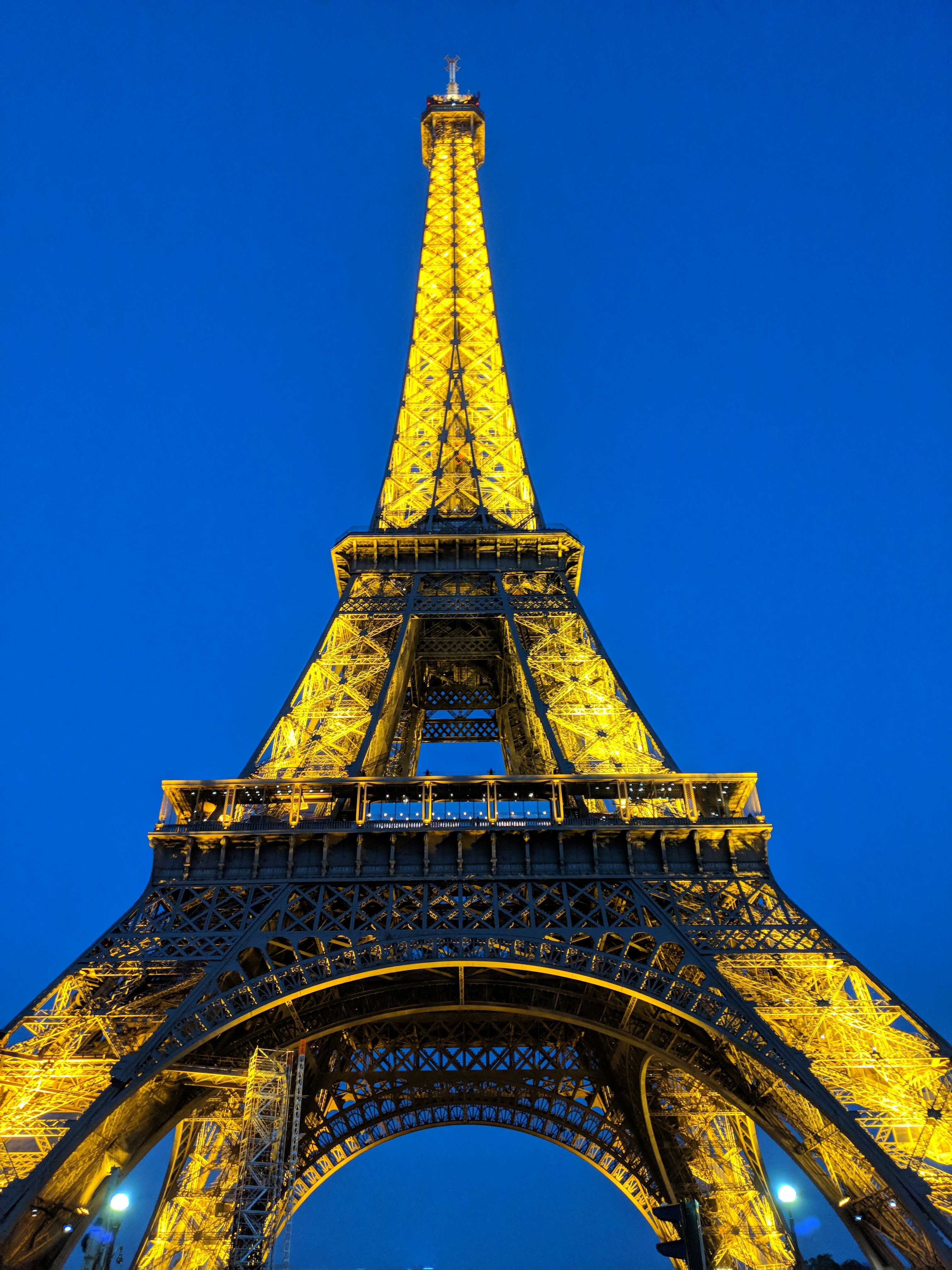 Eiffel Tower illuminated at night with golden lights reflecting on wet cobblestone street in deep blue dusk