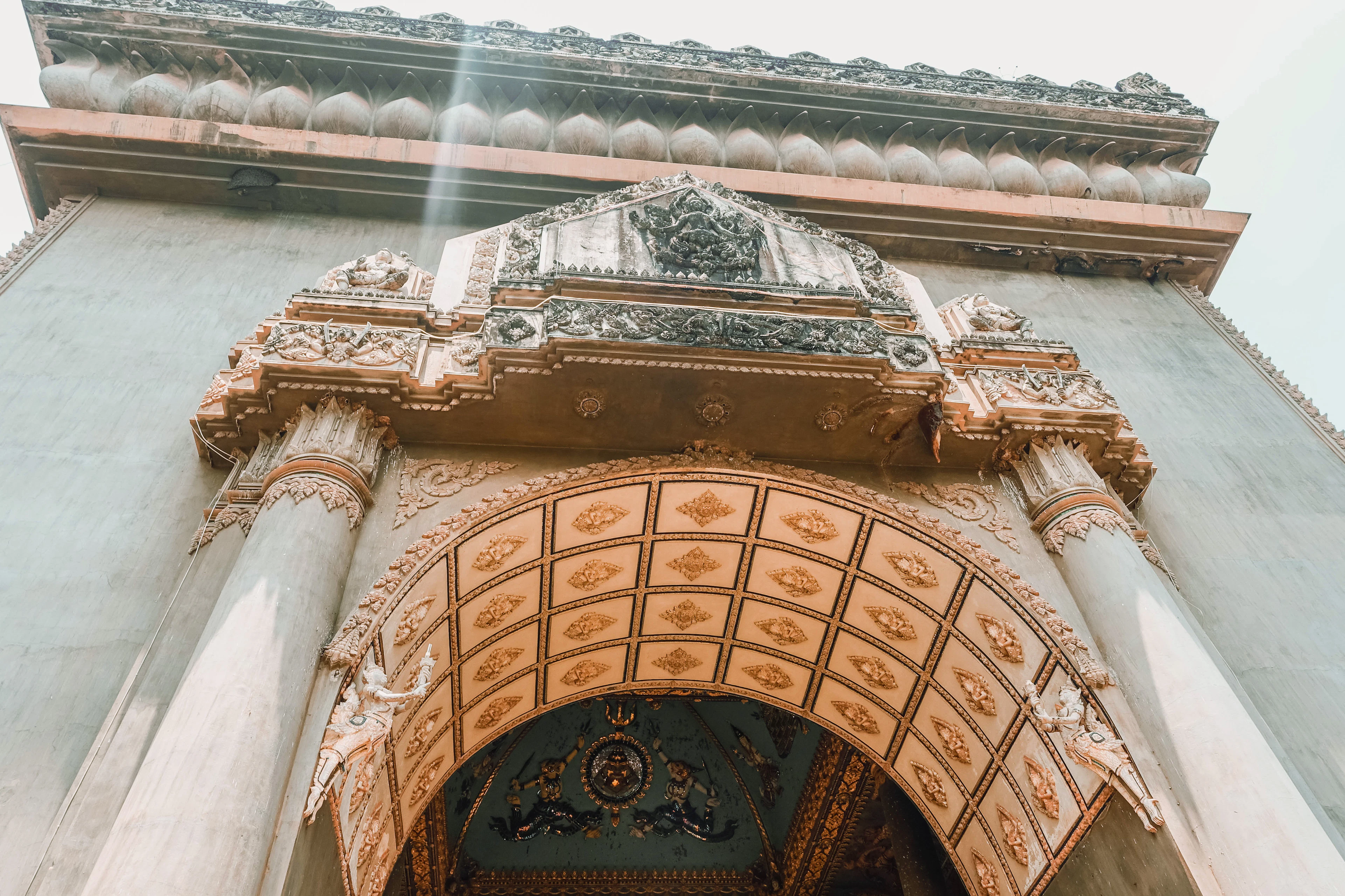 Looking up at the ornately decorated arch and carved ceiling of the Patuxai victory monument in Vientiane, Laos