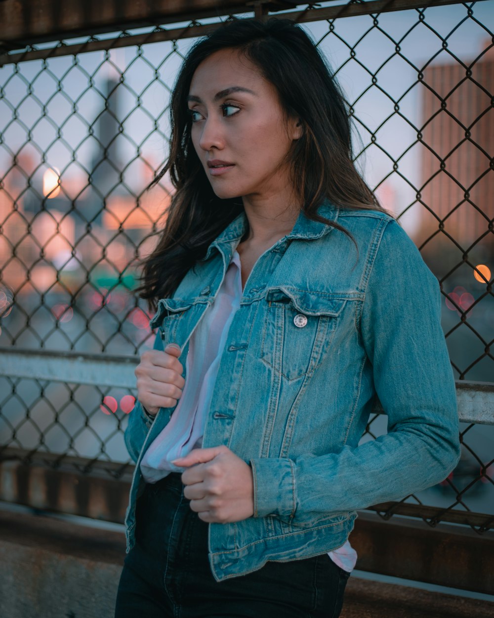 woman in blue denim jacket standing near black metal fence