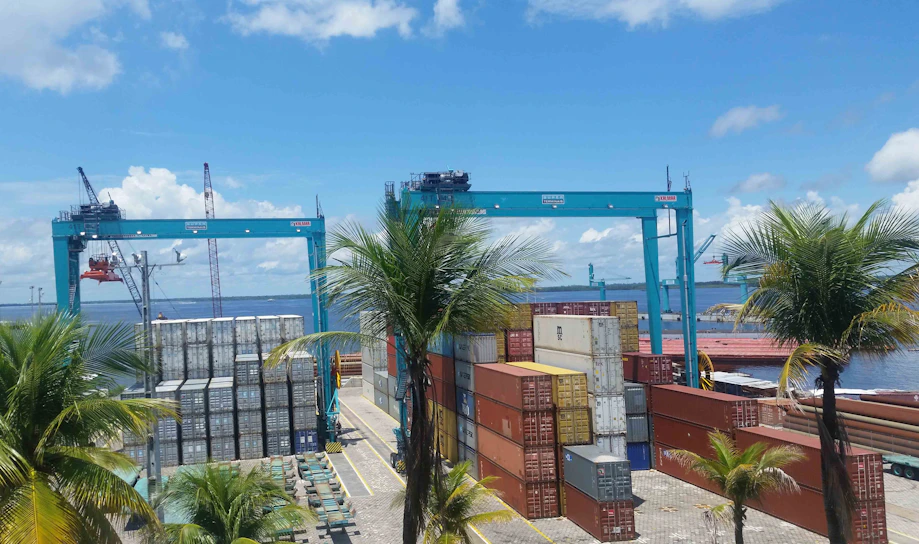 A cargo ship unloading containers at a busy UAE port under a clear blue sky.