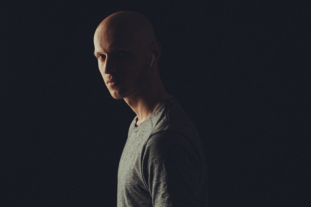 man wearing gray crew-neck shirt using Apple AirPods standing and facing his left side