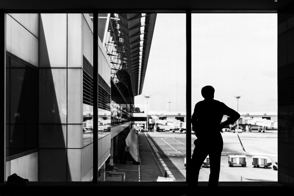 man standing beside glass window facing the field and buildings