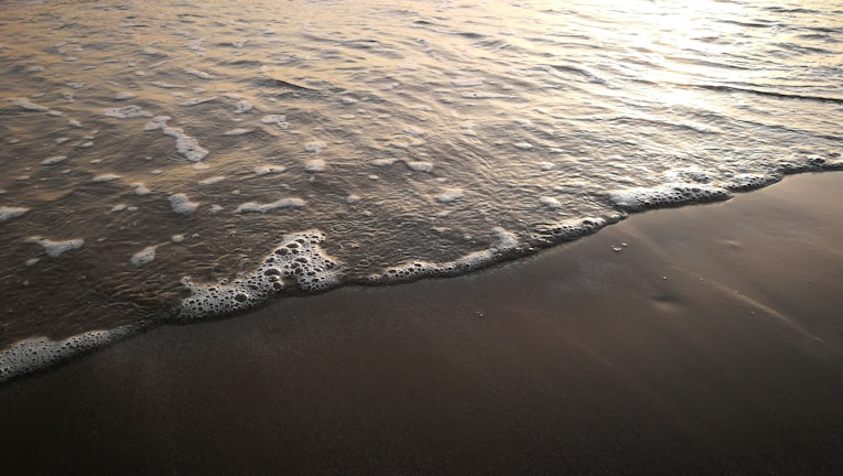 Slow-motion capture of waves gently crashing on a sandy beach.