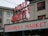A public market sign and farmers market sign in bright neon lights are displayed against the backdrop of an old building. The red letters are prominent with a large wall clock situated between the words. The building has multiple windows with red frames, contributing to an urban market scene.