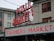 A public market sign and farmers market sign in bright neon lights are displayed against the backdrop of an old building. The red letters are prominent with a large wall clock situated between the words. The building has multiple windows with red frames, contributing to an urban market scene.