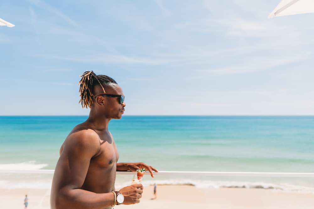uomo in topless che indossa occhiali da sole in piedi vicino alla riva del mare