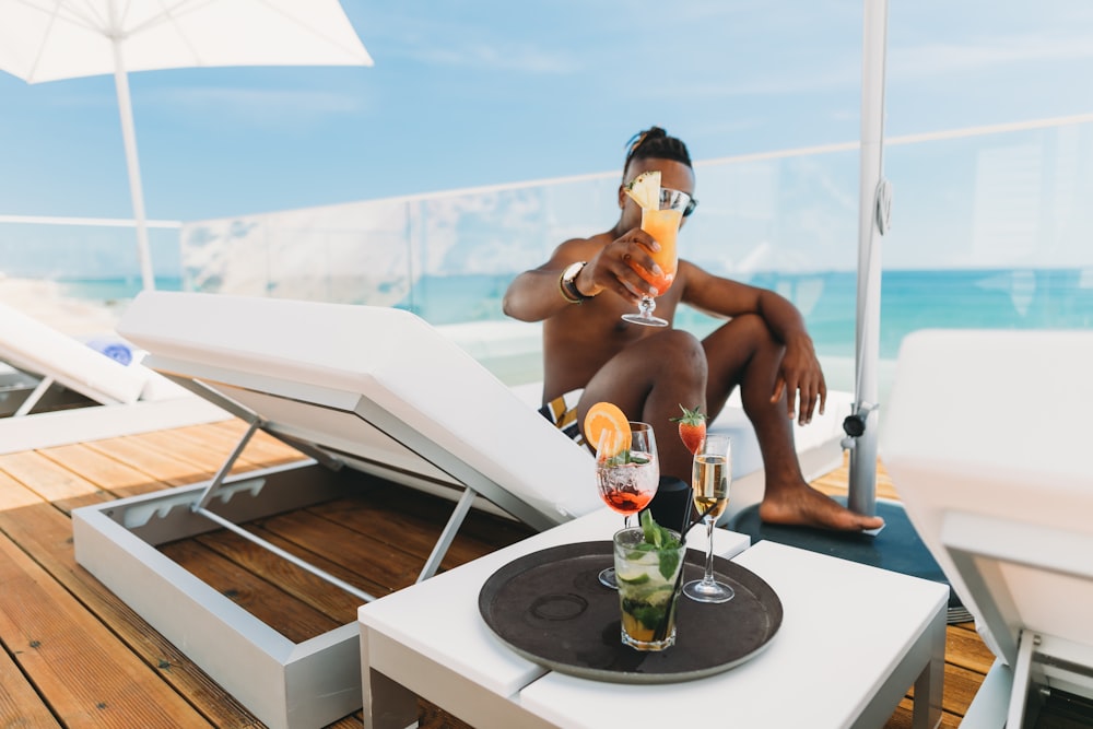 man sitting on lounge chair holding beverage filled drinking glass