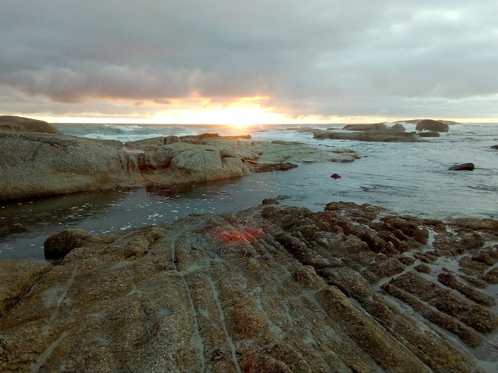 boulders in ocean under whcloudy sky