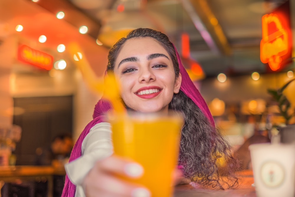 mulher na camisa branca de manga comprida segurando copo plástico laranja