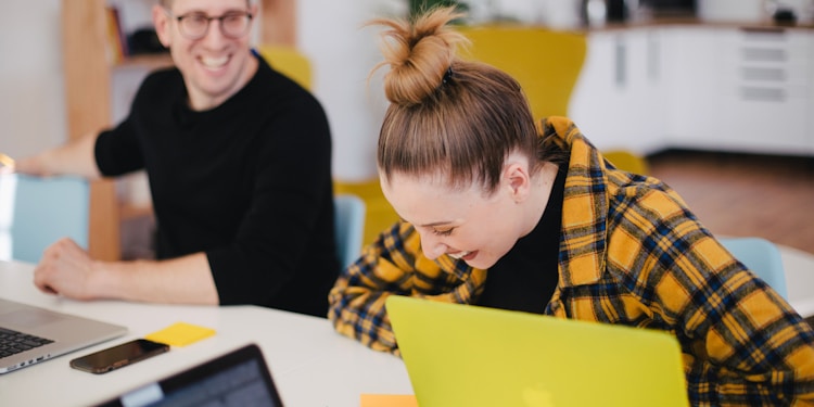 man and woman laughing while sitting in front of laptops