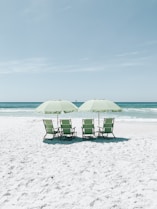 cadeiras verdes sob guarda-sóis de frente para o mar azul