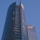 A modern high-rise building with a sleek glass facade and curved architecture against a clear blue sky. The structure features a prominent logo with the letters 'EY' on one of its sections.