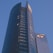 A modern high-rise building with a sleek glass facade and curved architecture against a clear blue sky. The structure features a prominent logo with the letters 'EY' on one of its sections.