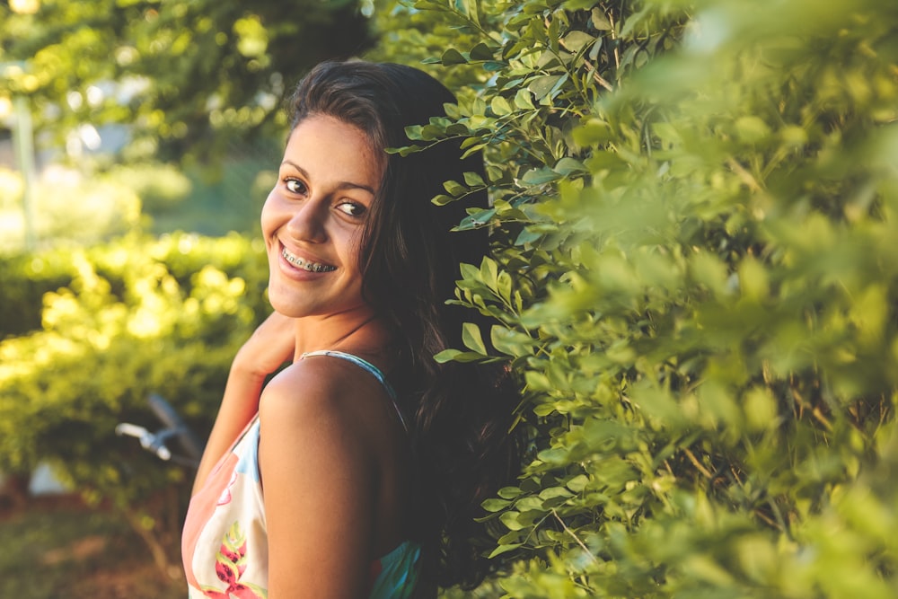 woman wearing spaghetti strap top leaning on grass hedge