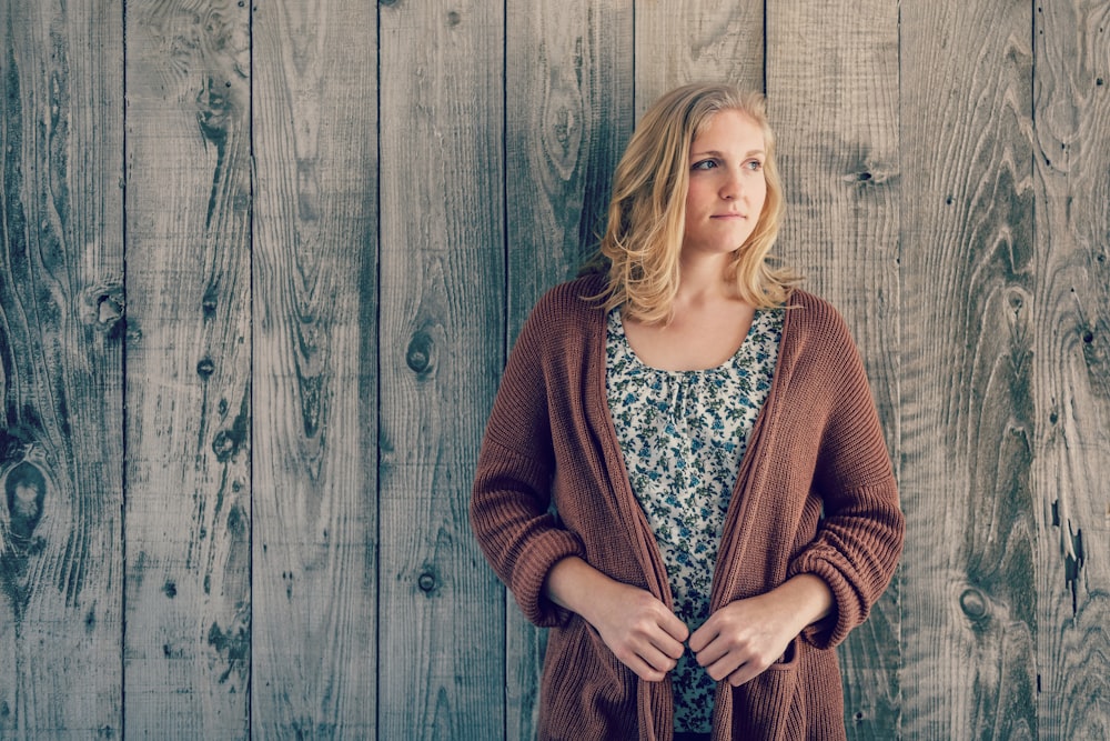 woman wearing brown cardigan leaning on wooden wall