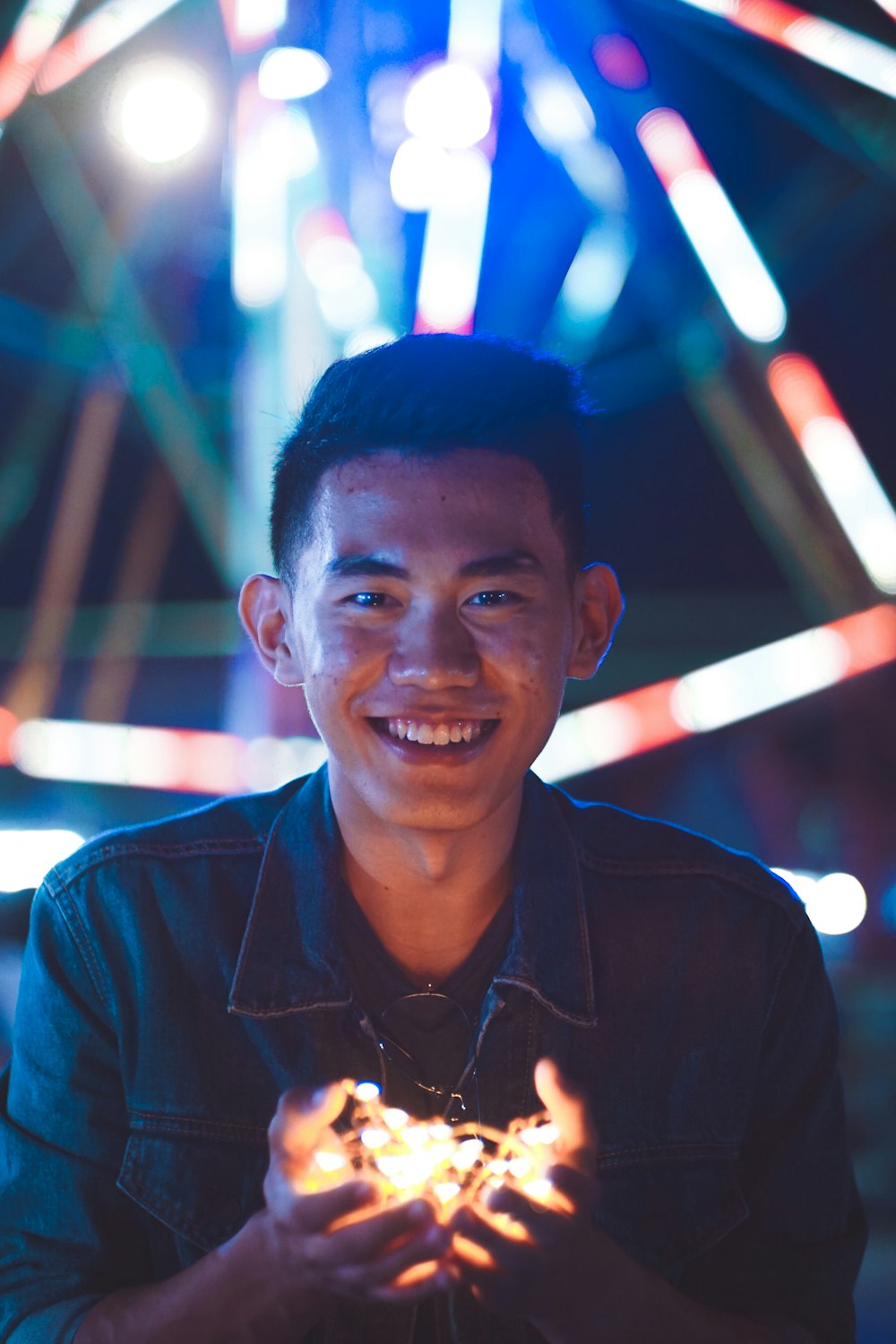 man in black jacket holding string lights smiling