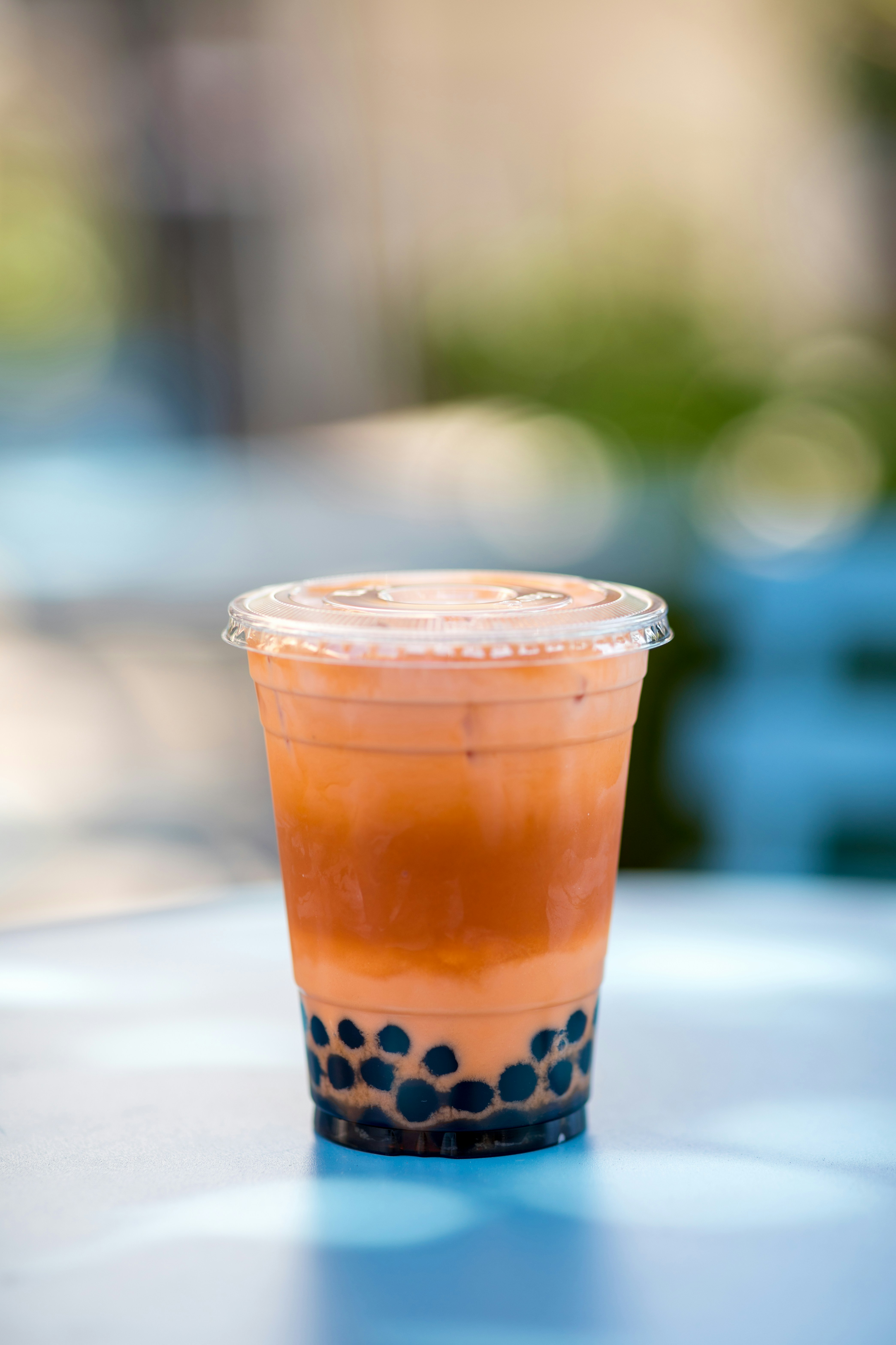 Row of colorful bubble milk tea drinks in clear cups with large black tapioca pearls and wide straws, vibrant pink and purple hues, dark stylish bar background