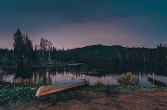 A serene lake at dusk with gentle lights lining a wooden dock and a canoe resting nearby.