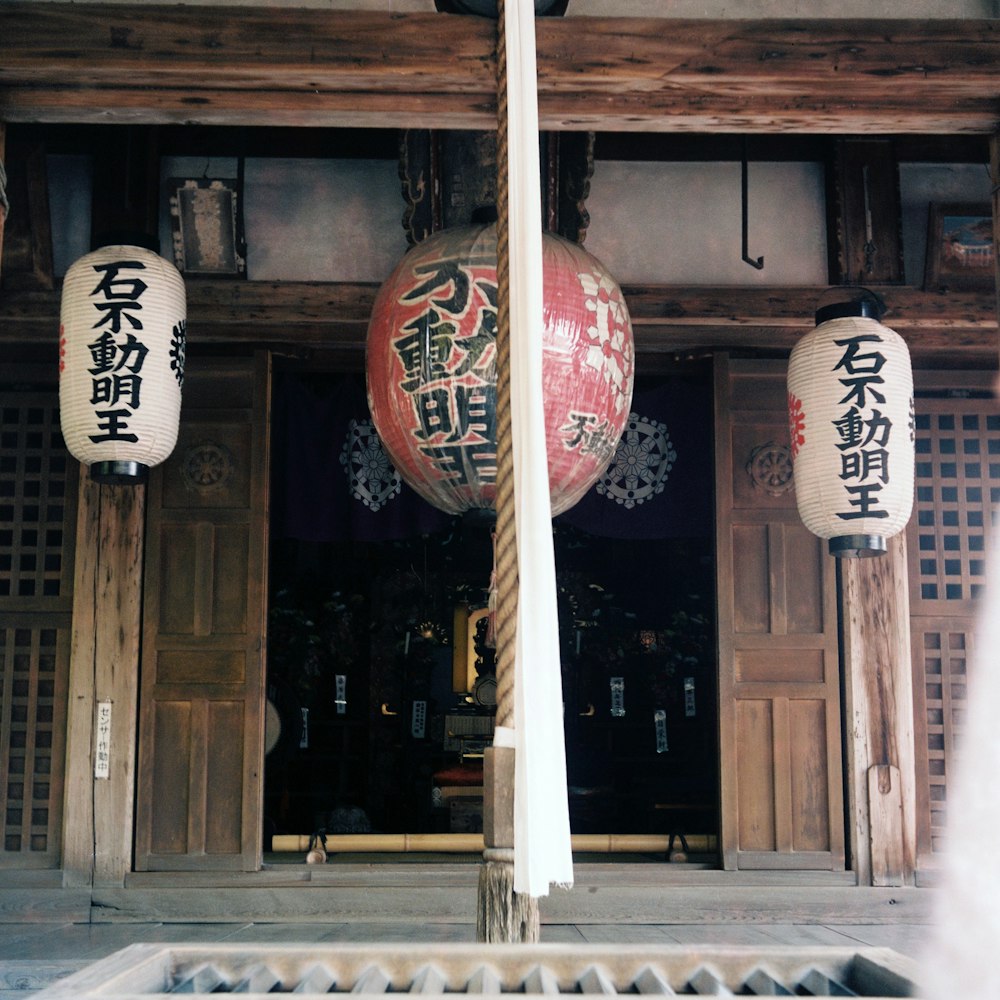 three hung red and white lanterns with kanji prints in front of opened door