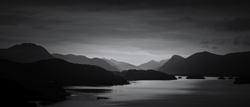 grayscale photography of body of water beside mountains