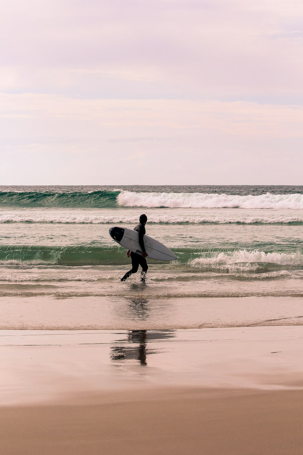 homme en chemise à manches longues blanche tenant une planche de surf blanche marchant sur la plage pendant la journée