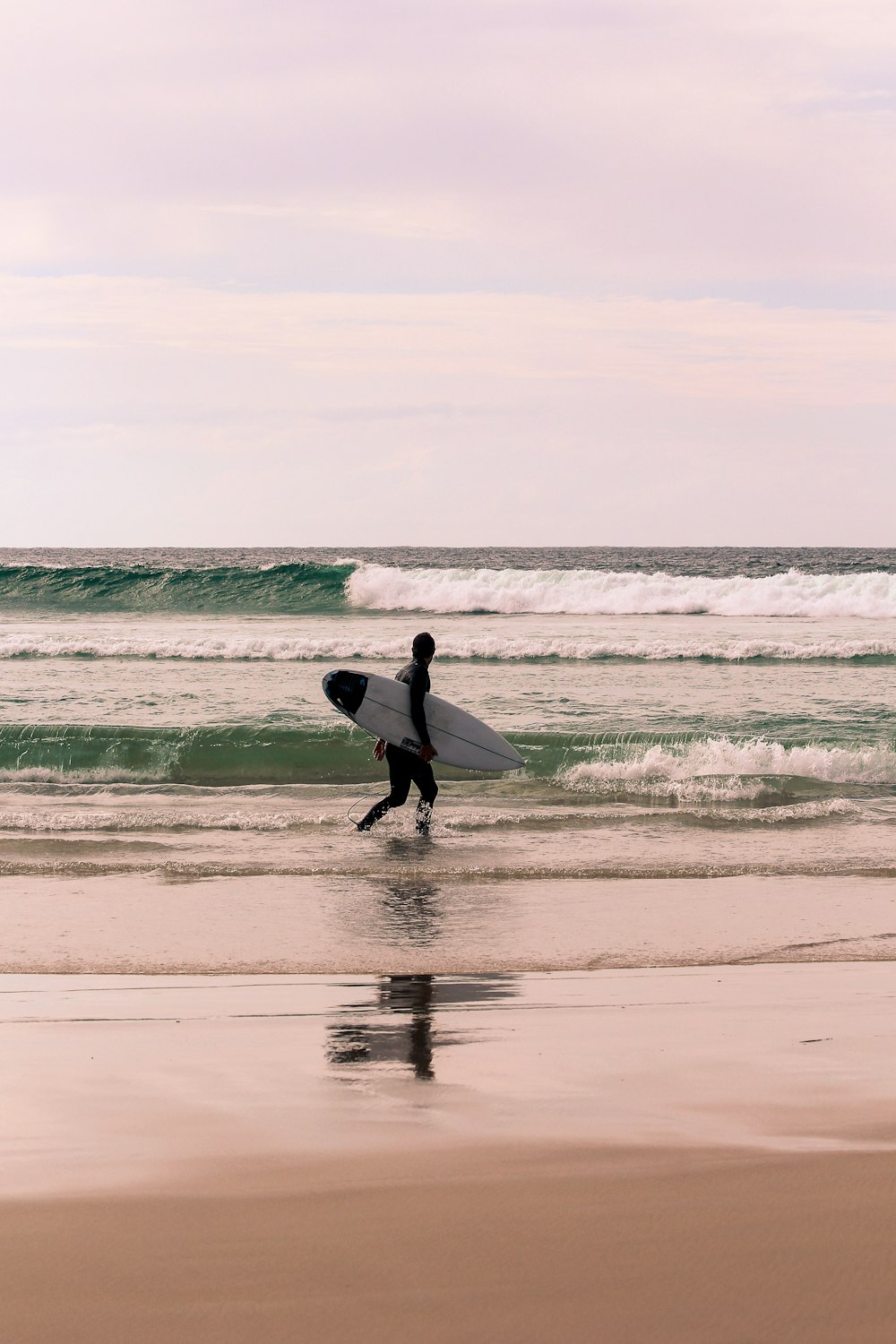 man in white long sleeve shirt holding white surfboard walking on beach during daytime