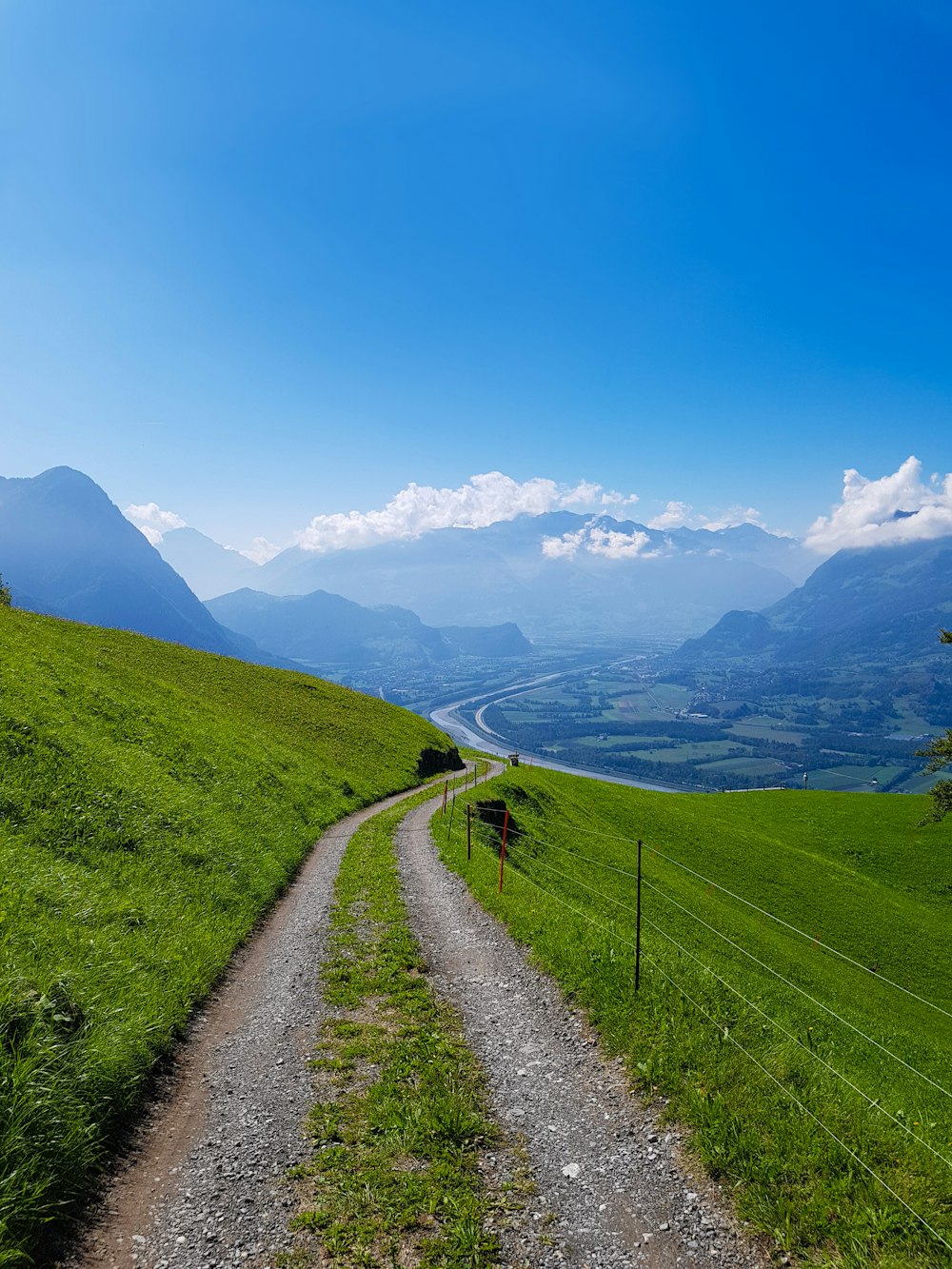 Mini strada grigia vicino alla montagna di osservazione del campo verde sotto cieli blu e bianchi