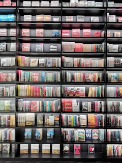 A large bookshelf filled with a variety of books stacked neatly in rows. The books have colorful spines with a mix of titles and authors visible. The shelf is black, creating a contrast with the diverse colors of the books.