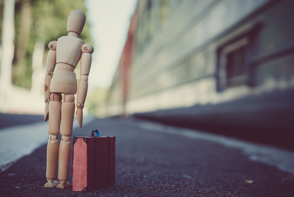 artist manikin standing beside suitcase toy on concrete floor