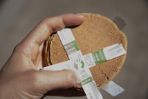 A hand is holding a stack of thin, round crackers secured with a white paper band that has green and Japanese text.