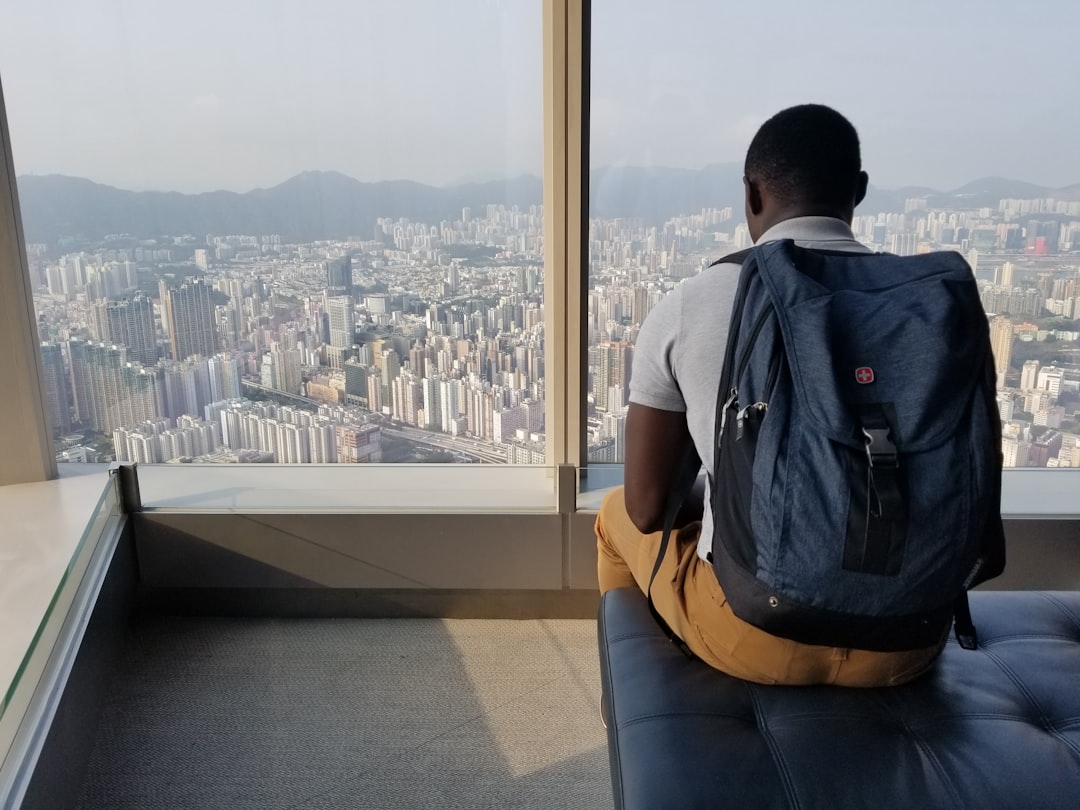 man sitting on sofa with blue backpack watching city during daytime