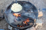 A compact camp cooking setup with a skillet and canteen on a rock.