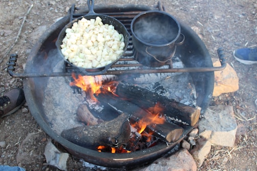 A compact camp cooking setup with a skillet and canteen on a rock.