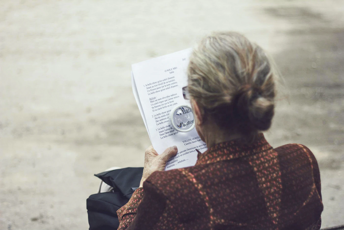 A person sitting outdoors on a bench reading a printed letter in daylight