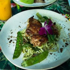 A vibrant platter featuring grilled chicken, veggie pasta, and fresh Caesar salad arranged beautifully on a rustic wooden table.