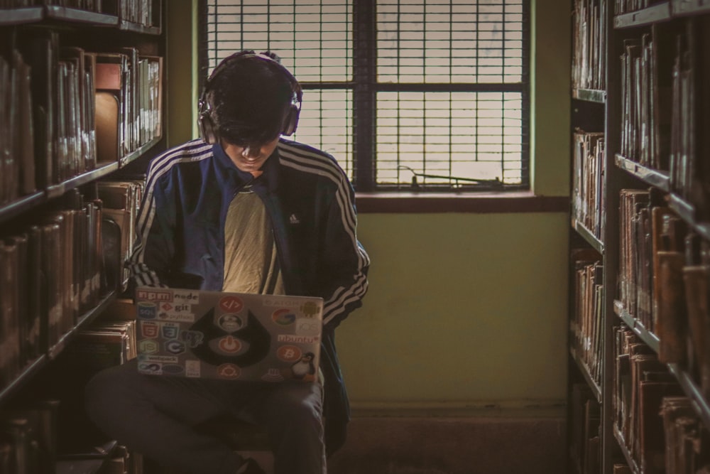 man using headphones sitting while using laptop inside library