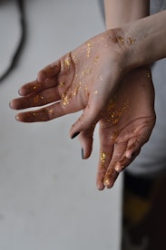 Hands showcasing glittery, custom press-on nails with a soft pink background.