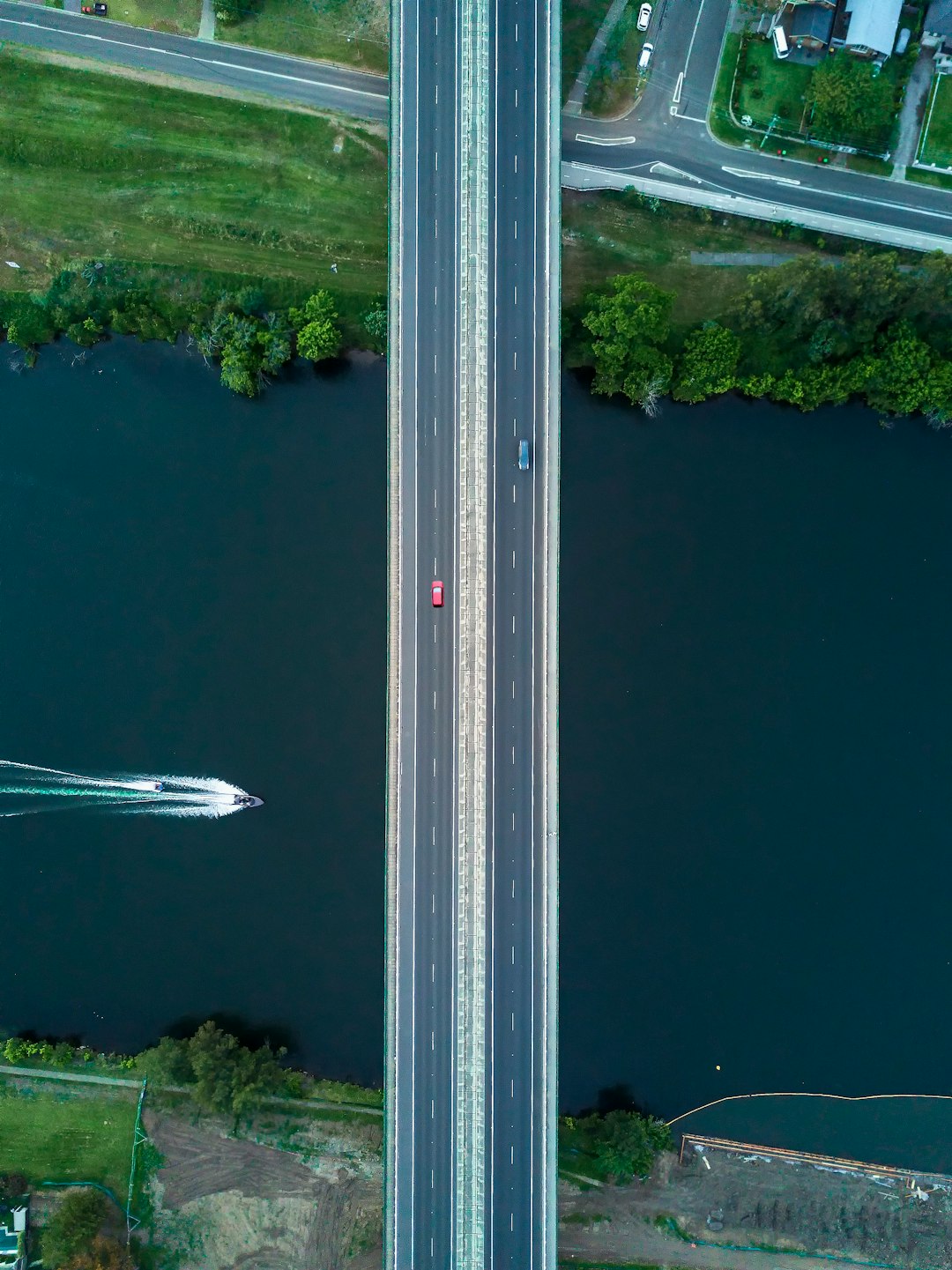 two vehicles passing on bridge viewing boat on lake