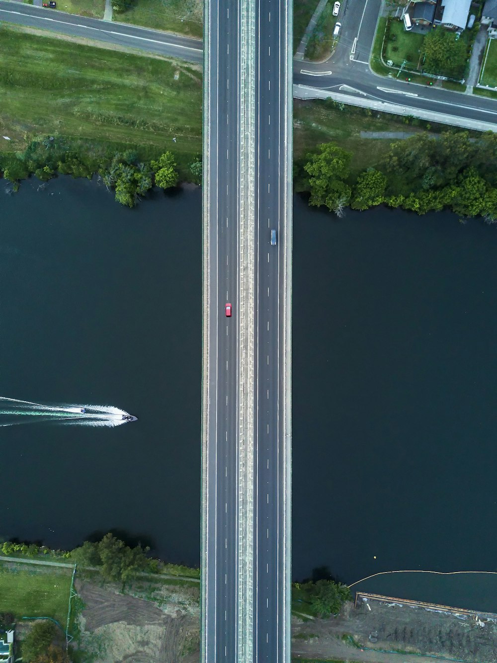 two vehicles passing on bridge viewing boat on lake